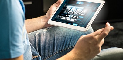 Excited man playing in an online casino with tablet fingers crossed wishing and hoping to win