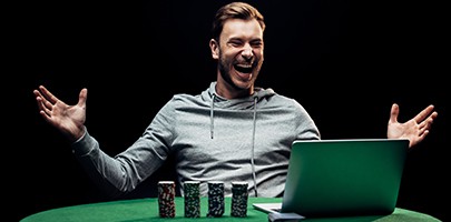 selective focus of happy man gesturing near poker chips near laptop isolated on black